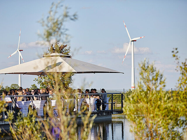 Auf der Terrasse der juwitality hat man Sicht auf Windräder. Sonnenschirmen spenden Schatten.